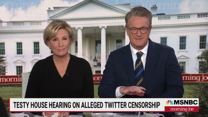 Two news anchors on a set with a white house backdrop and on-screen program text