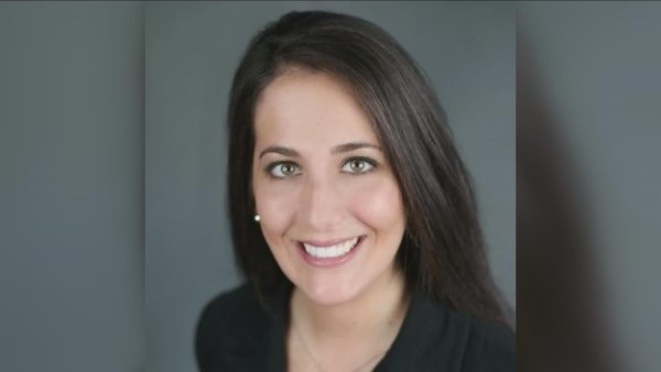 Smiling woman with shoulder-length dark hair in a dark blazer against a light background