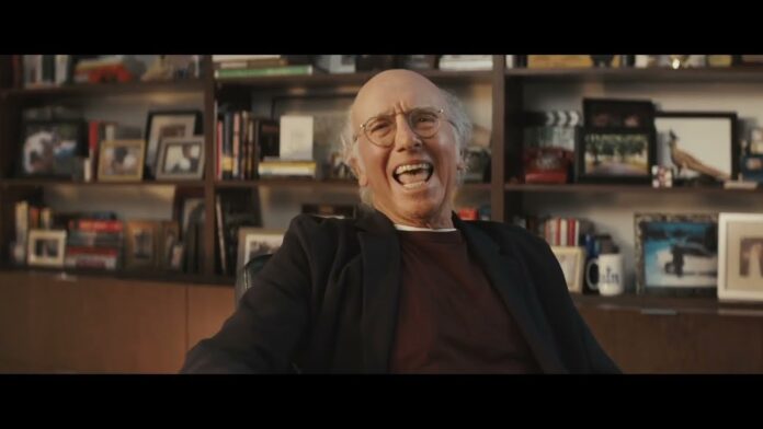 An elderly man laughs in a library-like room with bookshelves behind him.