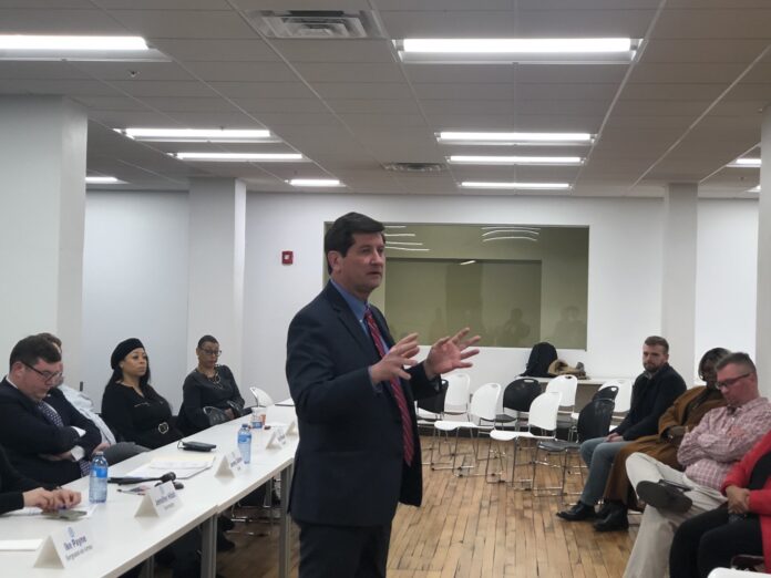 Man in suit gestures while speaking to seated people in a meeting room