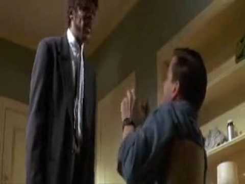 Two men stand indoors, one in a dark jacket and one in a blue shirt, gesturing.