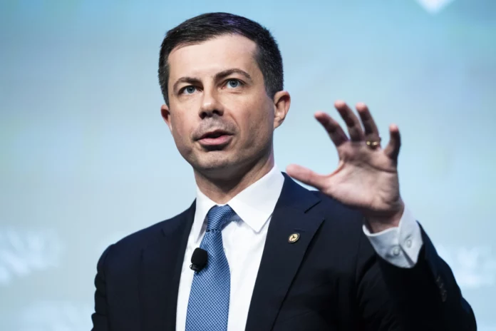 Man in a dark suit raises his hand while speaking against a blue backdrop