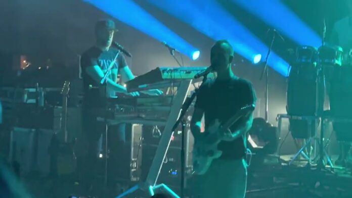 Musicians performing with guitars and keyboards under blue stage lights.