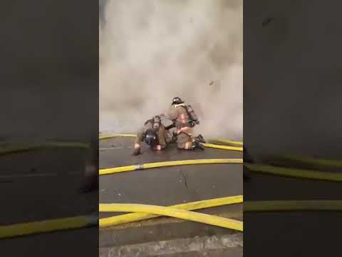 Firefighters in protective gear work near hoses amid heavy smoke