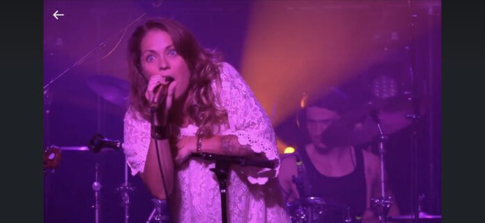 Performer singing into a microphone on a live stage with purple lighting