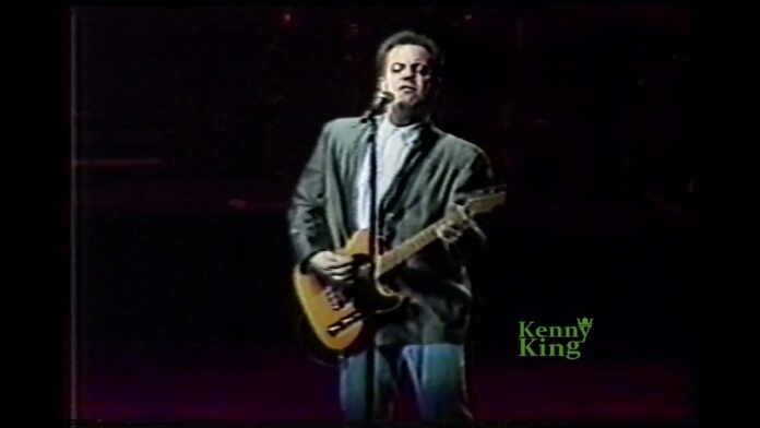 Performer in dark clothing singing into a microphone while playing an electric guitar