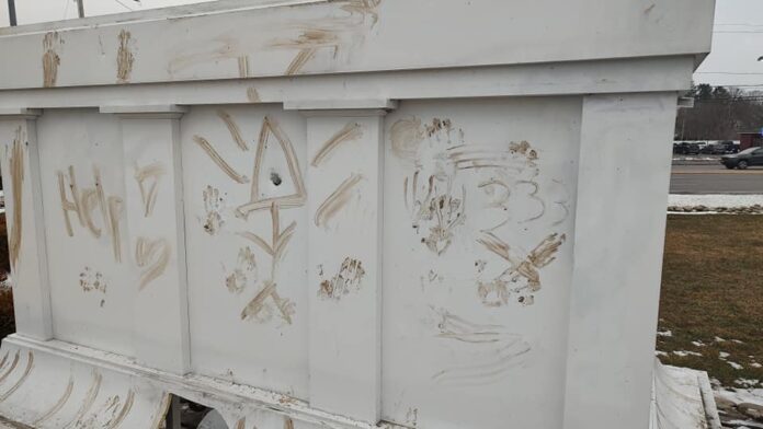 White outdoor structure with multiple gold-brown graffiti marks and scratches
