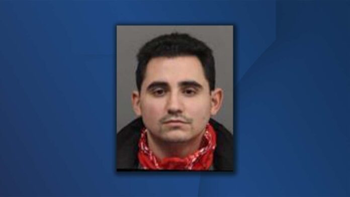 Mugshot-style portrait of a man in a gray background framed on blue newsroom graphic