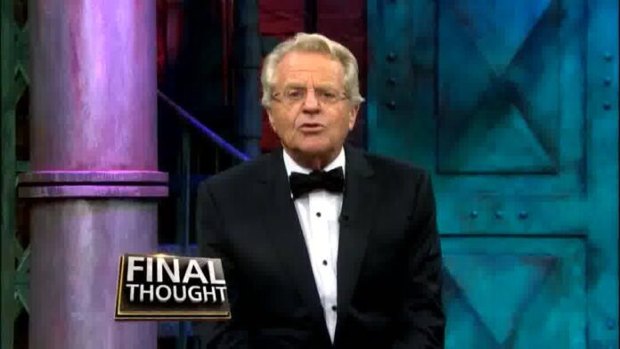Man in a tuxedo standing at a studio podium with a “FINAL THOUGHT” sign behind him.