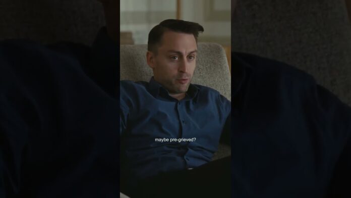 Man in dark shirt sits in a chair indoors, looking worried, with subtitle text on screen.