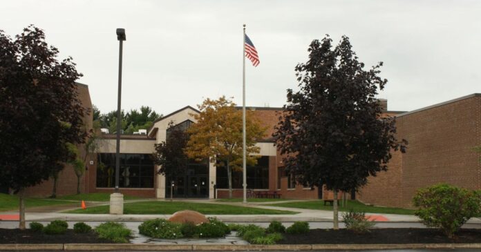 U.S. flag on a pole in front of a brick building with trees and walkway