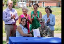 Waterkeeper and Army Corps Begin to Address Upper Scajaquada Creek People pose outdoors with a signed document and raised hands in front of a table.
