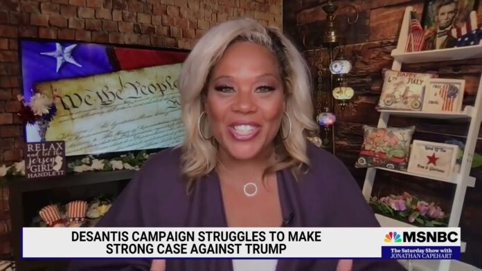 Smiling blonde news host in a studio with U.S. flag and a lower-third headline