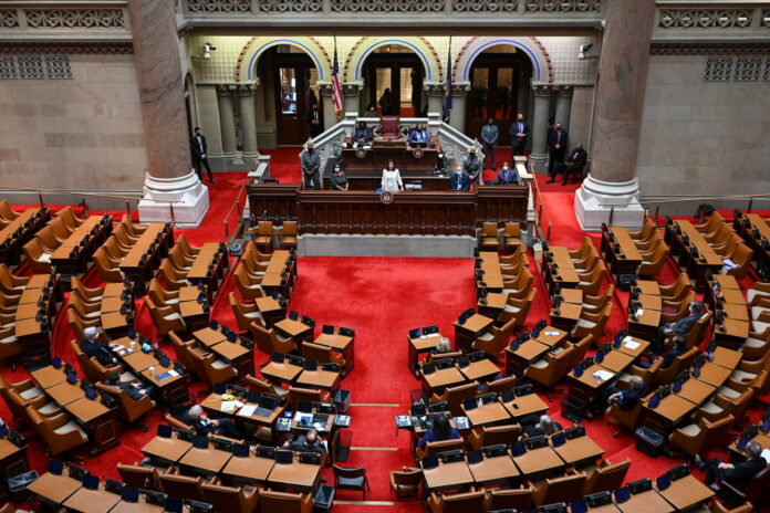Legislative chamber interior with rows of desks and chairs around a central podium.