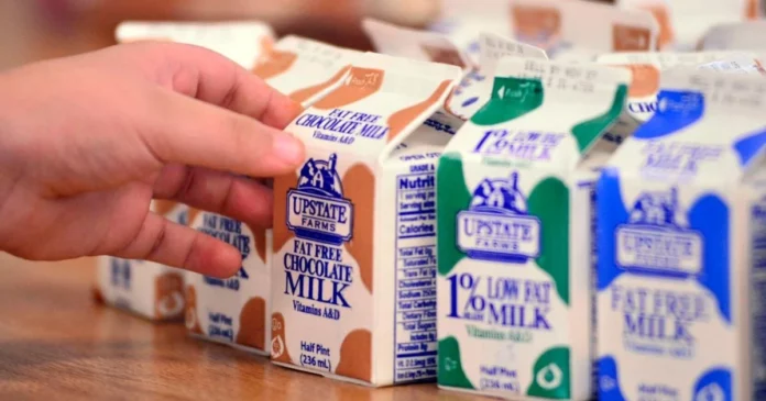 Hand grips an Upstate Farms fat free chocolate milk carton among other cartons