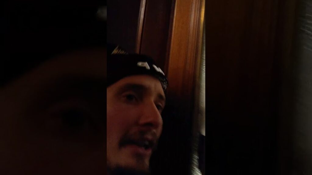 Man in a dark cap near a wooden door, seen in dim indoor lighting