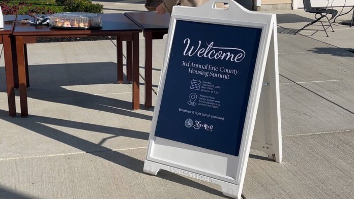 A welcome sign for the Erie County Housing Summit on a sidewalk outside a building