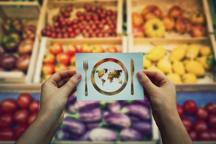Two hands hold a card with a globe inside a circle between fork and knife icons.
