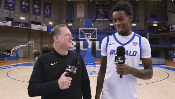 Athlete in a Buffalo basketball jersey being interviewed with a microphone at an indoor arena.