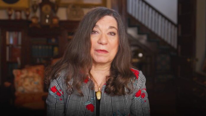 Woman with long dark hair wearing a checkered blazer with red floral accents