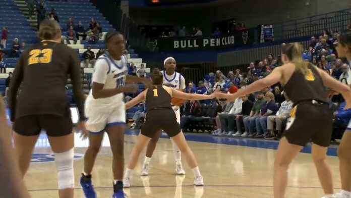 Women’s basketball players in uniforms stand on an indoor court near the Bull Pen Club sign.