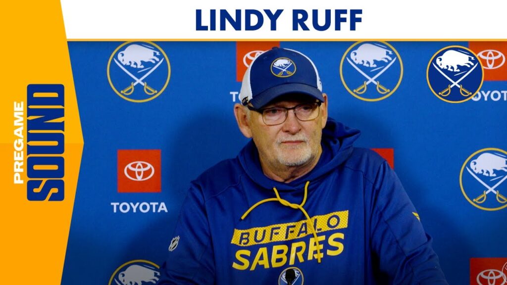 Coach wearing Buffalo Sabres hoodie and cap in front of team sponsor logos