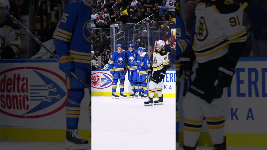 Buffalo Sabres players in blue and yellow stand together on the ice near the boards.