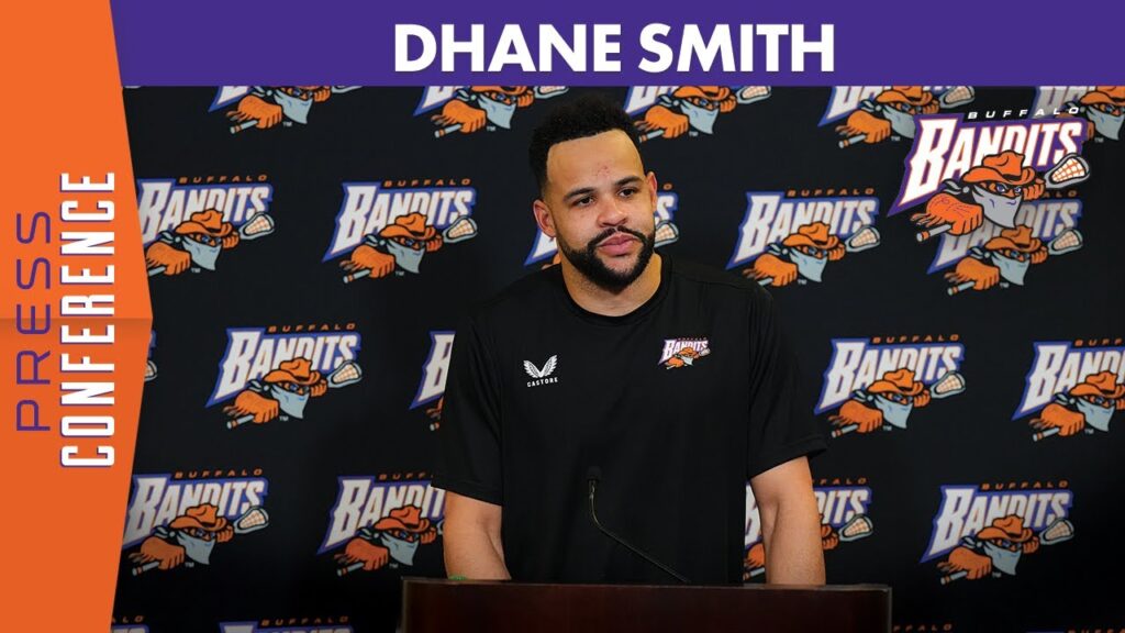 Man speaking at a podium in front of a Buffalo Bandits backdrop with repeated logos.