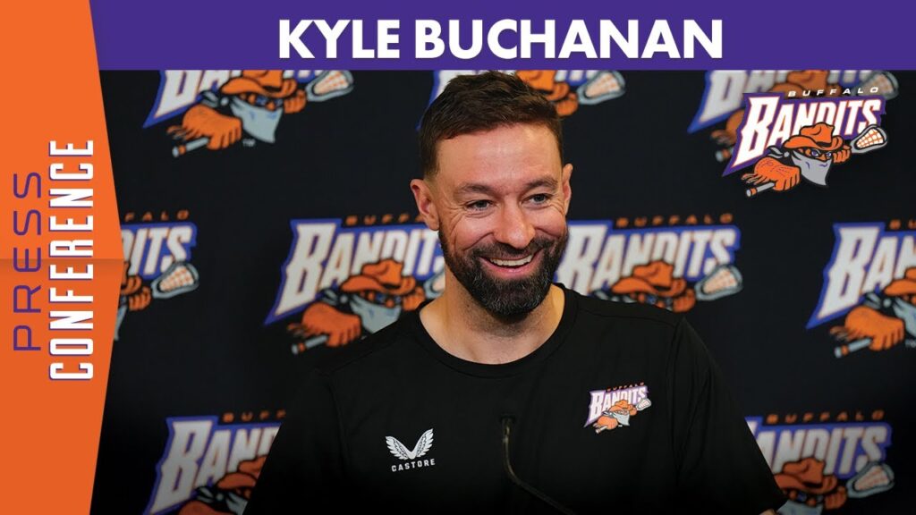 Kyle Buchanan smiling in front of a Buffalo Bandits logo media backdrop.