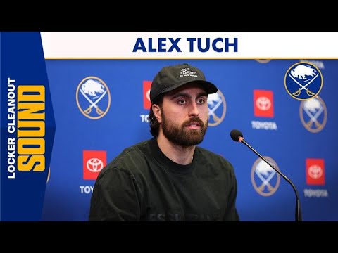 Man in a cap speaks at a press conference with a backdrop of sponsor logos.