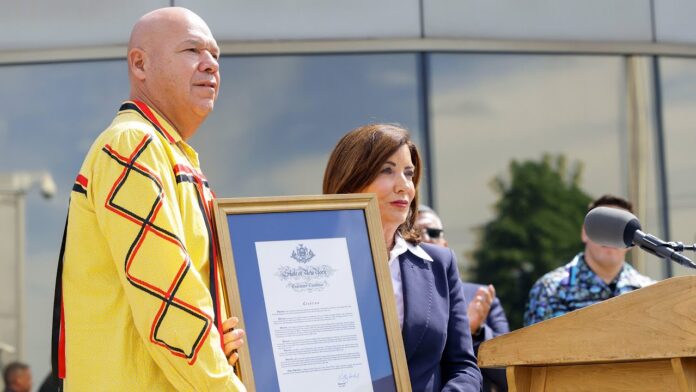 Officials stand at an outdoor podium holding a framed certificate during a ceremony.