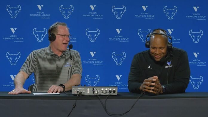 Two people wearing headsets sit at a table with microphones in a studio