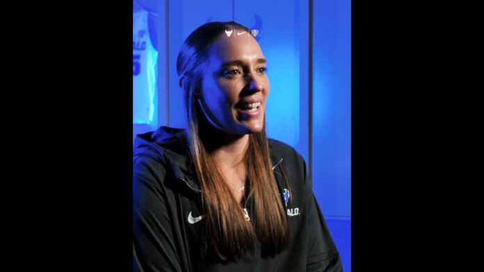 Woman in a black Nike jacket speaking during an interview under blue lighting.
