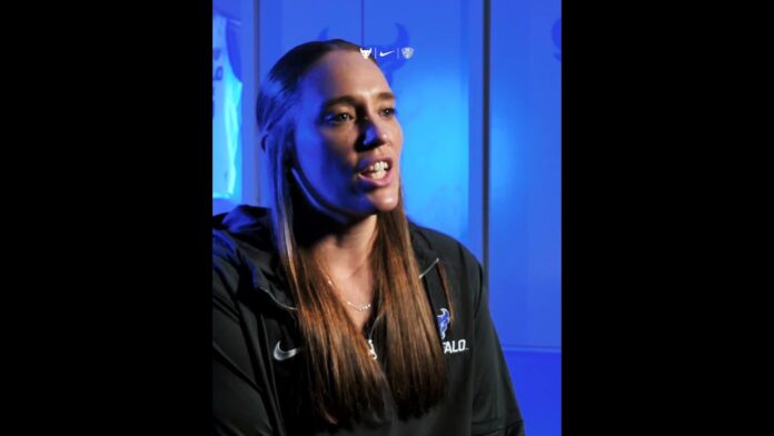Woman with long hair speaking during an interview in front of a blue-lit background